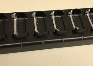Black rectangular base with six metal clamps arranged in a row, each clamp featuring a curved black end. Likely a mounting jig or clamp rack.