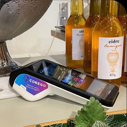 Point-of-sale card reader on a counter beside cider bottles in a shop setting.